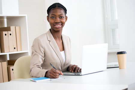 Portrait of pretty african-american business woman looking at camera at workplace in an officeの写真素材