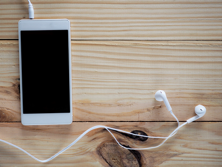 White headphones with smartphones on the wood table and free space for text and logo or symbols in the technology, communication and entertainment concept.の写真素材