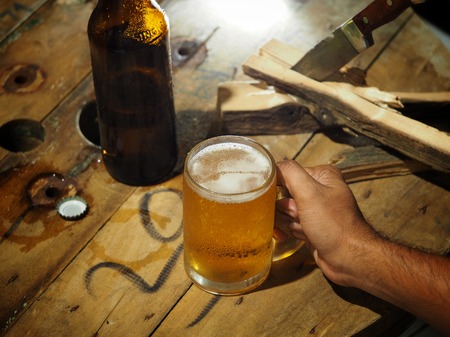 Beer in a glass and a bottle on a wooden table for work, with a knife and a log on the side.の写真素材