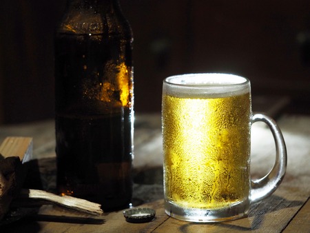 Beer in a glass and a bottle on a wooden table for work, with a knife and a log on the side.の写真素材