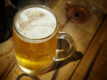Beer in a glass and a bottle on a wooden table for work, with a knife and a log on the side.の写真素材