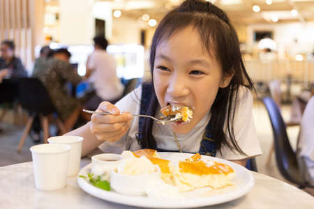 Attractive happy girl sitting and eating dessert,Close up portrait of a hungry greedy girl eating  pancake in the restaurantの写真素材