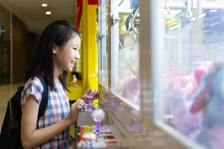 Asian girl playing Claw Game or cabinet catches the doll at one of the shopping mall outlets
