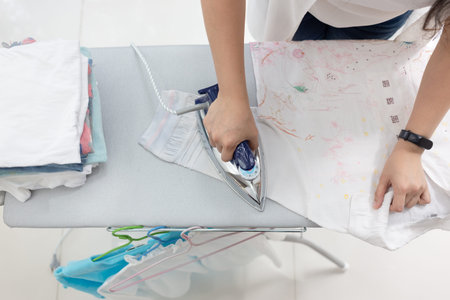 Woman ironing clothes using iron on ironing board at home,top view