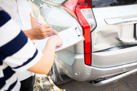 Insurance agent writing on clipboard while examining the car after accident claim was assessed and processed,traffic accident and insurance conceptの写真素材