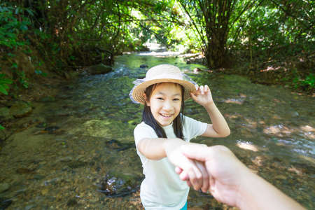 Asian girl in forest at stream,cute little girl studying and learning nature,natural forest background, girl having fun in trip near waterfall,smiling lovely,happy childhoodの写真素材