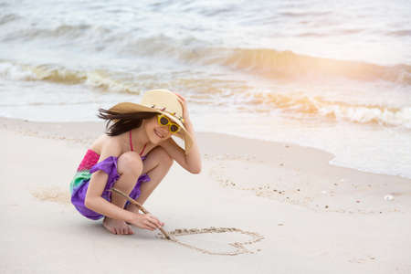 Asian girl draw heart shapes in the sand ,summer beach love conceptの写真素材