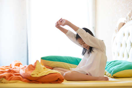Beautiful girl waking up in her bed,Asian girl smiling and stretching,healthy lifestyle,wellness conceptの写真素材