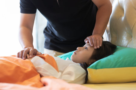 Asian girl feeling sick,female having headache and high temperature,cute little girl with father to care closely in the bedroom at home,medicine and health care concept.の写真素材