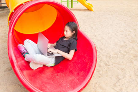 Asian girl is using a laptop in the playgroundの写真素材