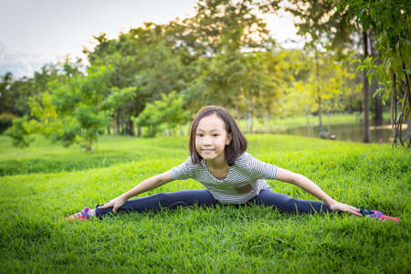 Asian little girl exercising at the outdoor park on the lawn is a meditation practice,child exercise in nature in the morning,healthy lifestyle conceptの写真素材