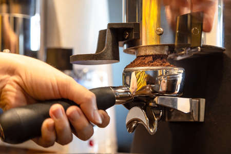 Close up woman hand holding portafilter, girl barista is grinding the roasted coffee beans into powder using coffee grinder at cafe shopの写真素材