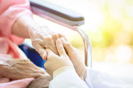 Closeup of hand medical female doctor or nurse holding senior patient hands and comforting her,Caring caregiver woman supporting disabled elderly people on wheelchair in outdoor park,help,health care conceptの写真素材
