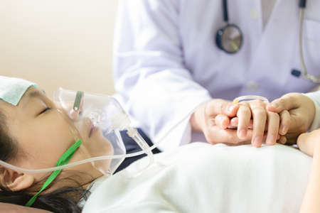 Closeup of hand female caregiver holding with little girl hands,cute child patient putting inhalation or oxygen mask in hospital bed or home,doctor or nurse intensive care,health care,support,help conceptの写真素材