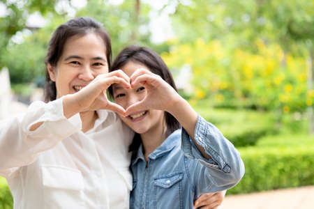 Happy beautiful asian adult woman and cute child girl forming a heart with their hands while hugging and smiling in garden,love of mother with her little daughter in outdoor park in nature,motherâs day, family, love conceptの写真素材