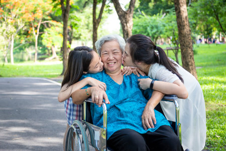 Asian daughter and granddaughter are kissing their smiling elderly grandmother on her both cheeks in...