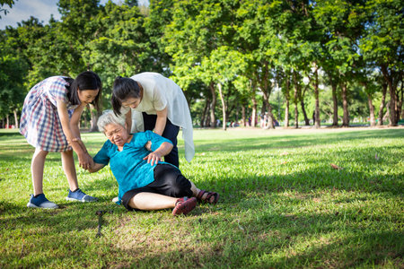 Asian elderly people with walking stick on floor after falling down and caring young woman caregiver,assistant or daughter,granddaughter to help and take care of her in summer outdoor,sick senior woman or mother fell to the floor because of dizziness,faint,suffering from illnessの写真素材