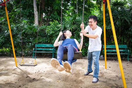 Happy asian little child girl having fun,enjoy,playful,playing on the swing,beautiful daughter riding on swing in playground,smiling father pushing,dad swinging her in outdoor park,vacation family conceptの写真素材