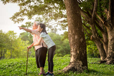 Happy asian little child girl support,hug senior grandmother,smiling granddaughter in outdoor park,elderly woman with walking stick,walk fun talk,watching something in nature,family health care, love conceptの写真素材