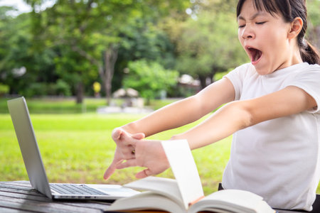 Asian little child girl stretching and bored while reading book,female student with laptop computer...