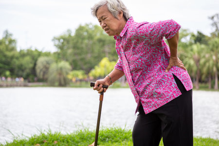 Asian senior woman with hip joint pain while walking in nature in summer,female patient having...