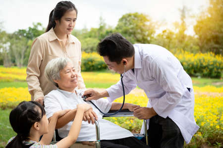 Male asian doctor examining senior woman patient by stethoscope, family doctor checking using stethoscope to listening breath,heart beat sounds lungs of elderly people,general health checkup,health care conceptの写真素材