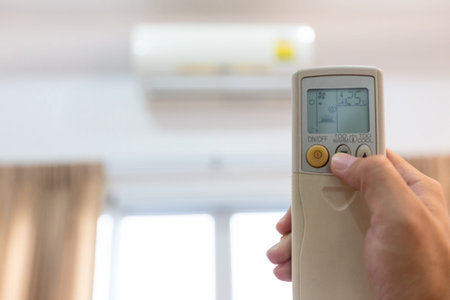 Woman holding a remote control with air conditioner,controlling the temperature,adjust air conditioner to 25 degrees celsius,energy saving campaign,save electricity bill and environment,global warmingの写真素材