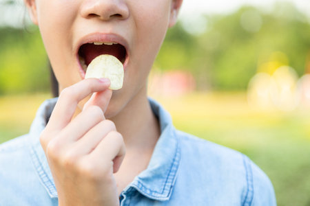 Closeup,bad food,asian little child girl eating potato chips,young woman puts crisps potato chip in...