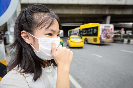 Asian child girl with face mask protection while walking on the street,person wearing medical mask because of air pollution in the city,allergy to dust,dirty air prevent PM 2.5,protecting health conceptの写真素材