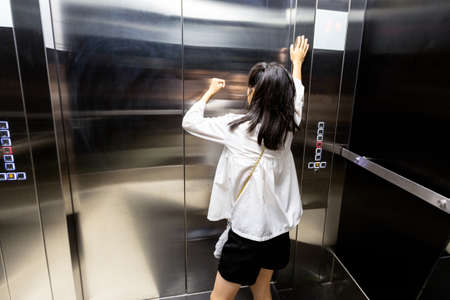 Shocked asian child girl is stuck in an elevator,sad teenager girl standing alone and screaming in a despair suffering from claustrophobia in the elevator,worried woman is experiencing fear,stress,anxiousの写真素材