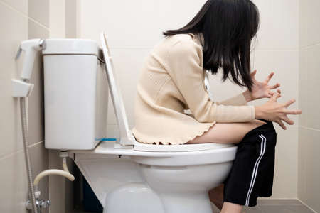 Asian child girl sitting on toilet with her pants down in the bathroom with suffering from constipation,diarrhea or hemorrhoids,anxiety woman feel painful stomach,couldnât get the poo out,health careの写真素材