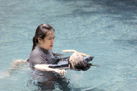 Asian child girl drowning in underwater,drowning female teenager in swimming pool,mother rescuing unconscious daughter drowning in swimming pool in dangerous situation,concept of safetyの写真素材