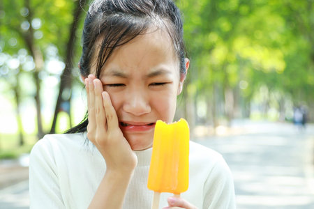 Asian child girl have hypersensitive teeth eating ice-cream,feel painful ,female teenage have...
