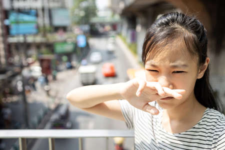 Asian child girl catches her nose because toxic fumes from car,bad smell,air pollution,dust allergies or sinus infection,female teenage rubbing nose suffer from allergic in city,life of urban peopleの写真素材