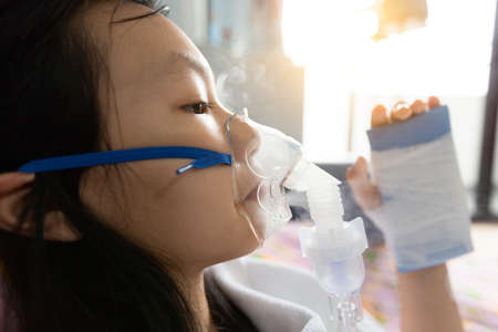 Closeup of sick asian child girl wearing oxygen mask has problems with the respiratory disease,treatment from oxygen therapy,female patient put inhalation suffer from asthma,influenza virus in hospital bed,health care,medical conceptの写真素材