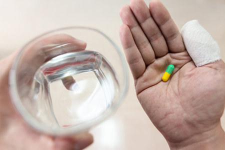 Male patient have capsule pill in hand with water from glass and thumb fingers with injured bandage...
