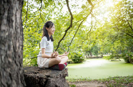 Happiness woman meditating in yoga pose or lotus position under the tree in green nature,asian child girl practicing yoga meditation in outdoor park,relax time,calmness,meditation ,healthcare conceptの写真素材