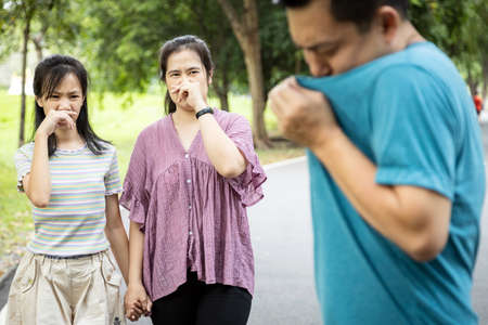 Asian man check his own smell,sniffing his wet armpit or sweating a lot because of hot weather or after exercise,husband bad smell while wife and daughter closing her nose,child girl feel stinksの写真素材