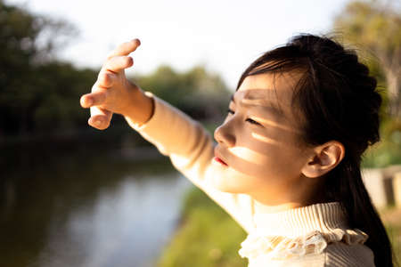 Asian child girl covering face by hand to protect,prevent face skin from bright sun in outdoor summer,female people hand covered the strong sun light feeling hot uncomfortable,risk of eyes damageの写真素材