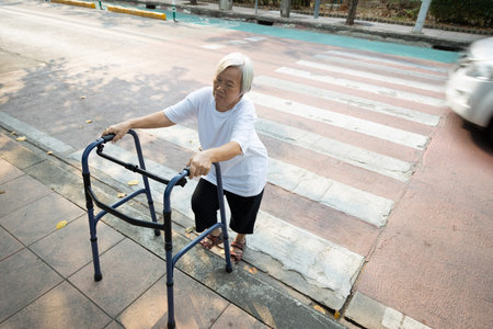 Asian senior woman was trying to walk up the sidewalk with walker after cross the road on crosswalk,...