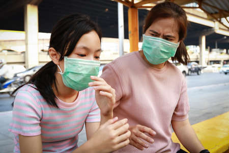 Tired asian child girl with hygienic mask sitting at bus stop,feel sick,woman wearing face mask protection,dirty air prevent PM2.5,air pollution,allergy to dust,bad smell from cars in city Bangkokの写真素材
