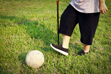 Healthy asian senior woman exercising with old soccer ball,active female elderly with walking stick,...