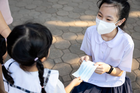 Generous girl student in Thai school uniform with mask,schoolgirl is sharing protection mask with...