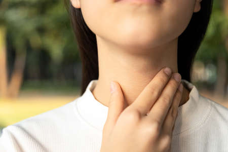 Closeup of hands of asian female people holding her inflamed throat or tonsillitis,child girl touch the neck with her hands,woman has fever,sore throat pain irritation,hard to swallow or loss of voiceの写真素材