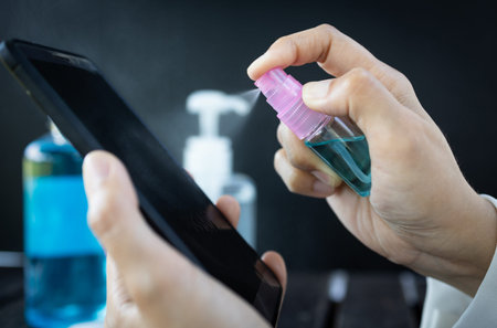 Hand of woman is spraying alcohol,disinfectant spray on mobile phone,prevent infection of Covid-19...