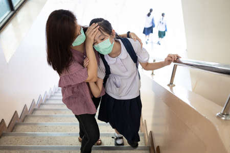Exhausted asian child girl with illness and fever,girl wear face mask,has vertigo,dizziness or symptoms of the Coronavirus,Covid-19 infection,flu and cold,feel tired,sick woman is fainting unconsciousの写真素材