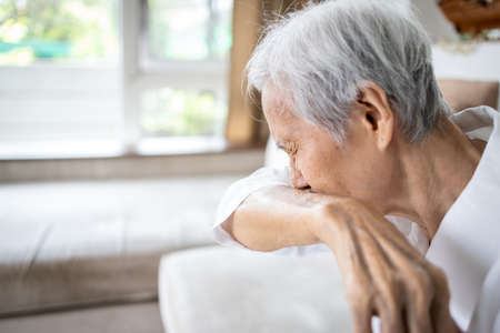 Asian elderly people with sneezing,coughing into her sleeve or elbow to prevent spread Covid-19,Coronavirus,sick senior woman has fever covering nose,mouth with her arm,infectious symptoms of flu,coldの写真素材
