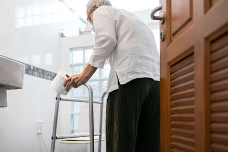 Senior woman with diarrhea holding tissue roll near a toilet bowl,elderly have abdominal pain,stomach ache,constipation,sick people use walker to walk to the bathroom,belly diarrhea,irritable bowelの写真素材