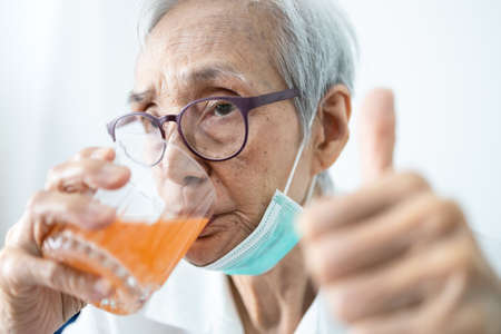 Healthy asian senior woman is drinking a glass of vitamin C or orange juice,elderly people with effervescent vitamin C,strengthening the immunity for cold,flu,fight the Coronavirus,against of Covid-19の写真素材