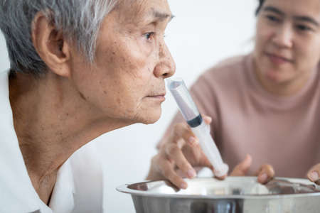 Nasal irrigation,asian caregiver is helping senior woman wash away dirt her nasal,nose cleaning,elderly people having allergic to weather,irrigation prevent allergies,air pollution,smog,dust of PM2.5の写真素材